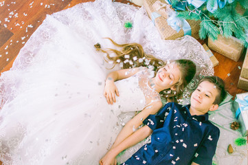The elder brother and sister with long hair in a beautiful white dress near the Christmas tree...