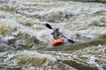  Kayaking in very rough rapids. The river is violent with a lot of turbulent waves and spray. The face of the person in the kayak is not identifiable due to the spray in front of him. 