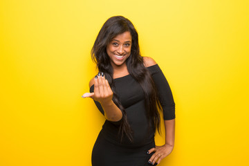 Young afro american woman on vibrant yellow background inviting to come with hand. Happy that you...