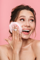 Pretty young woman posing isolated over pink wall background holding powder puff.