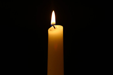 tiny wax glowing yellow candle with vivid fire against the heavy black background.