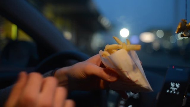 A man eats a French Fries Potato from McDonalds sitting in a Car at Night