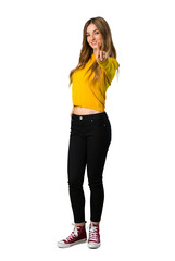 A full-length shot of a young girl with yellow sweater showing and lifting a finger on isolated white background