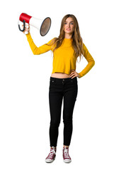 A full-length shot of a young girl with yellow sweater taking a megaphone that makes a lot of noise on isolated white background