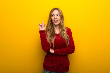 Young girl on vibrant yellow background thinking an idea pointing the finger up