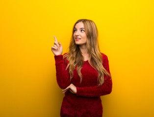 Young girl on vibrant yellow background pointing a great idea and looking up