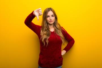 Young girl on vibrant yellow background showing thumb down sign with negative expression
