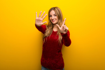 Young girl on vibrant yellow background counting seven with fingers