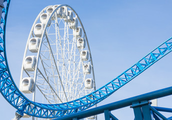 Ferris wheel and Loop turn on a blue roller coaster in an amusement park.