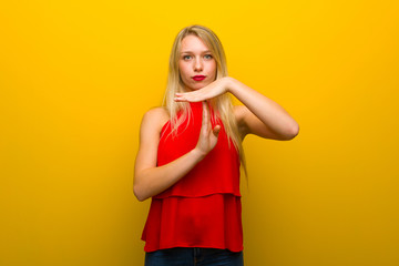 Young girl with red dress over yellow wall making stop gesture with her hand to stop an act