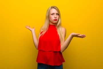 Young girl with red dress over yellow wall unhappy and frustrated with something because not understand something