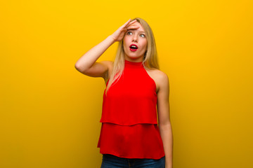 Young girl with red dress over yellow wall with surprise and shocked facial expression