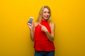 Naklejka premium Young girl with red dress over yellow wall showing the mobile