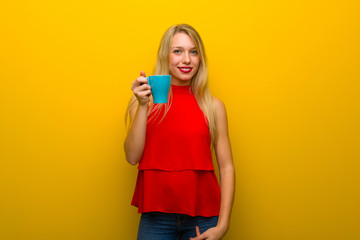Young girl with red dress over yellow wall holding a hot cup of coffee