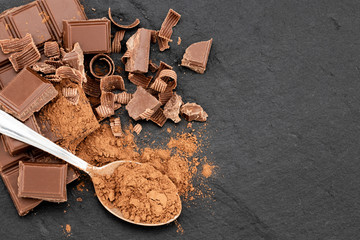 Broken chocolate pieces and cocoa powder on a dark background. Top view with copyspace for your text