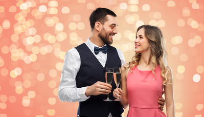 celebration and people concept - happy couple with champagne glasses toasting over living coral background and festive lights