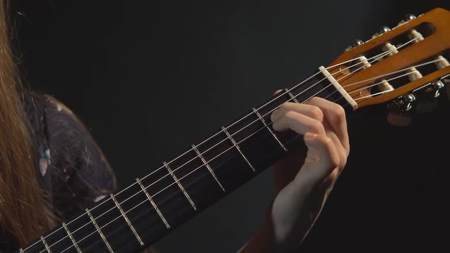 Girl play guitar. Closeup. Studio light. Dark background.
