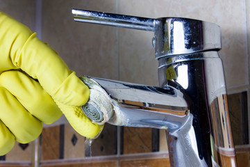 Hand in  yellow glove repairs faucet aerator,  limescale on  tap mixer.