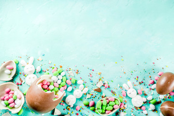 Obraz na płótnie Canvas Colorful spring easter sweets background, with chocolate eggs, sugar sprinkles and marshmallow bunny, turquoise light blue concrete background copy space top view