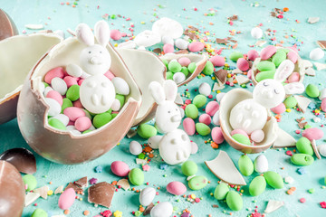 Colorful spring easter sweets background, with chocolate eggs, sugar sprinkles and marshmallow bunny, turquoise light blue concrete background copy space top view