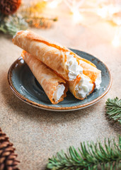 Traditional Christmas Norwegian cookies Krumkake with whipped cream among winter decor.