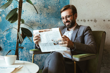 Smiling businessman wearing suit reading newspaper
