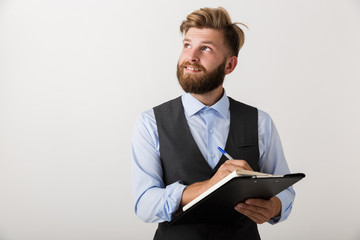 Handsome young bearded man standing isolated over white wall background holding clipboard.
