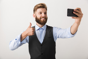 Handsome young bearded man standing isolated over white wall background take a selfie by mobile phone.