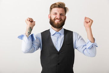 Excited young bearded man standing isolated over white wall background make winner gesture.