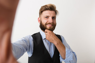 Young bearded man standing isolated over white wall background make selfie by camera.