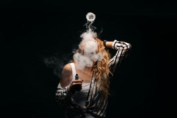 Redhead woman vaping electronic cigarette with smoke on black background closeup. Young woman...
