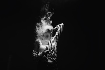 Redhead woman vaping electronic cigarette with smoke on black background closeup. Young woman smoking e-cigarette to quit tobacco. Vapor and alternative nicotine free smoking concept, copy space 