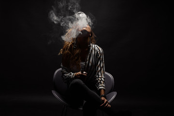 Redhead woman vaping electronic cigarette with smoke on black background closeup. Young woman smoking e-cigarette to quit tobacco. Vapor and alternative nicotine free smoking concept, copy space 