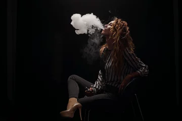 Papier Peint photo Lavable Fumée Redhead woman vaping electronic cigarette with smoke on black background closeup. Young woman smoking e-cigarette to quit tobacco. Vapor and alternative nicotine free smoking concept, copy space 