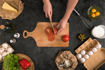 cropped view of woman chopping tomatoes on cutting board with pizza ingredients on grey background