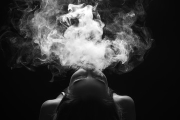 Redhead woman vaping electronic cigarette with smoke on black background closeup. Young woman smoking e-cigarette to quit tobacco. Vapor and alternative nicotine free smoking concept, copy space 