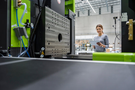 Businesswoman in high tech company controlling manufacturing machines, using digital tablet