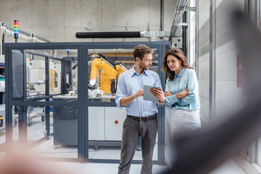 Colleagues In High Tech Company Controlling Industrial Robots, Using Digital Tablet