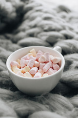 Delicious sweet marshmallows in white cup on knitted plaid
