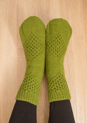 A woman wearing warm hand craft socks. Knitted from a natural sheep wool yarn. Winter clothing. On a wooden background.