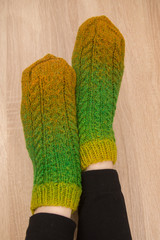 A woman wearing warm hand craft socks. Knitted from a natural sheep wool yarn. Winter clothing. On a wooden background.