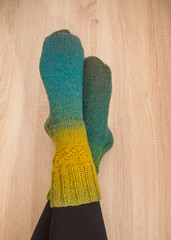 A woman wearing warm hand craft socks. Knitted from a natural sheep wool yarn. Winter clothing. On a wooden background.