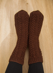 A woman wearing warm hand craft socks. Knitted from a natural sheep wool yarn. Winter clothing. On a wooden background.