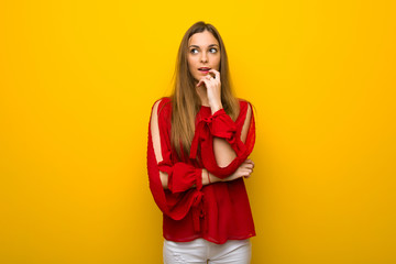 Young girl with red dress over yellow wall having doubts while looking up