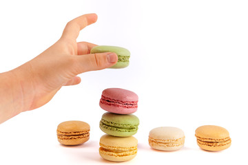 Child's hand placing green macaron on tower of colorful French macarons on white background