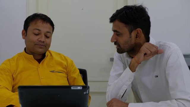 Two colleagues celebrate after achieve their goal and target asa group on a touchscreen electronic tablet and shake hands 