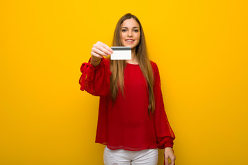 Young girl with red dress over yellow wall holding a credit card