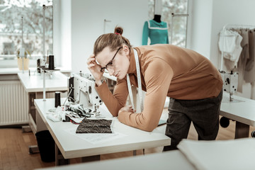 Long-haired fashion dressmaker in a brown garment looking thoughtful