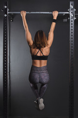 Woman athlete executing pull up in gym