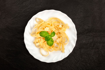 A plate of Italian pasta with Parmesan cheese and basil leaves, shot from the top on a black...
